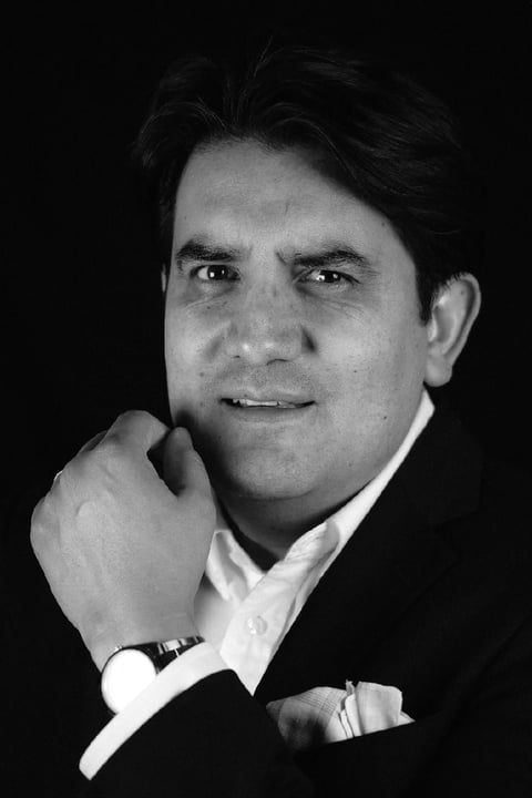 Black and white portrait of a man in formal attire with hand near face, against dark background